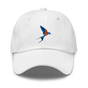Puede incluir: Gorra de béisbol blanca con un diseño de pájaro azul y naranja bordado.