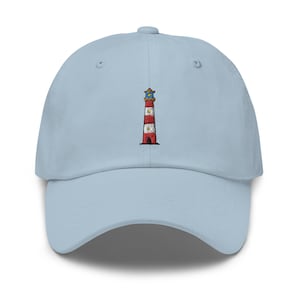 Può includere: Un cappellino da baseball azzurro con un ricamo centrale raffigurante un faro. Il faro presenta strisce orizzontali rosse e bianche, un tetto marrone e un piccolo dettaglio luminoso giallo sulla sommità, cucito sulla parte anteriore.