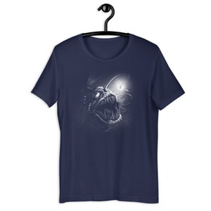 K&ouml;nnte beinhalten: Ein marineblaues T-Shirt mit einem wei&szlig;en Aufdruck eines Tiefsee-Anglerfisches mit einer biolumineszierenden Angel.
