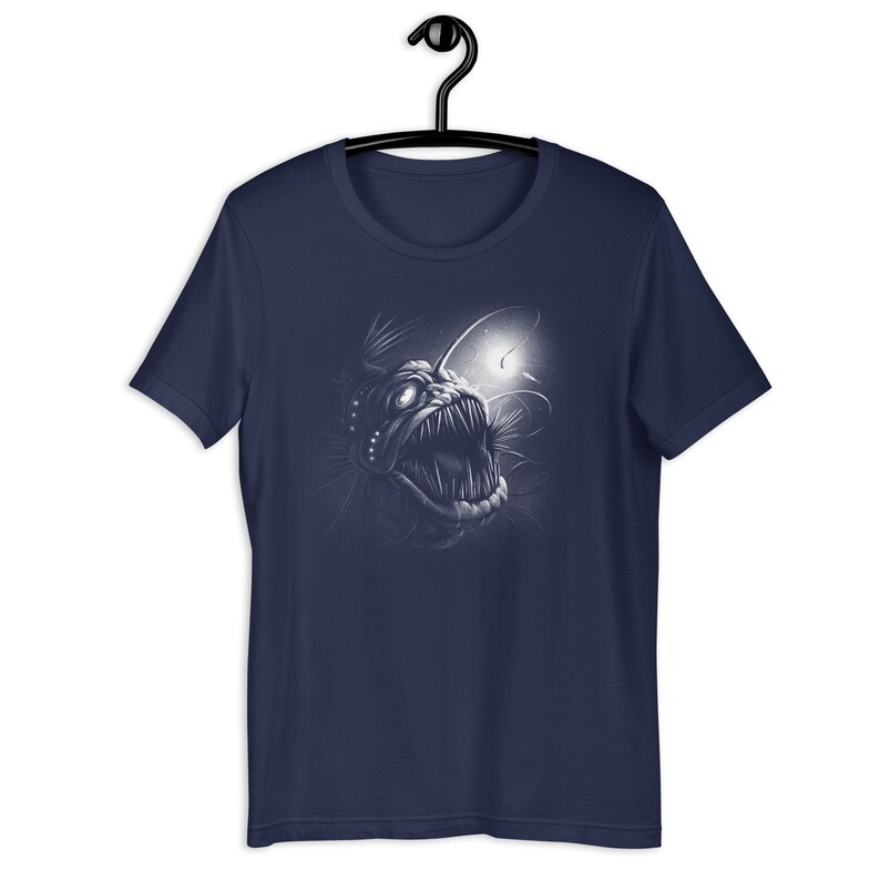 K&ouml;nnte beinhalten: Ein marineblaues T-Shirt mit einem wei&szlig;en Aufdruck eines Tiefsee-Anglerfisches mit einer biolumineszierenden Angel.