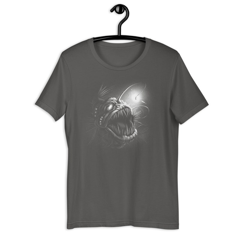 K&ouml;nnte beinhalten: Ein dunkelgraues T-Shirt mit einem wei&szlig;en Grafikdruck eines Anglerfisches mit scharfen Z&auml;hnen und einem biolumineszierenden K&ouml;der.