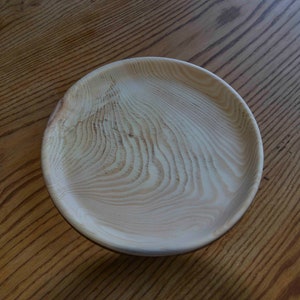Può includere: Un piatto rotondo in legno di colore marrone chiaro con un motivo a venature del legno naturale.