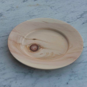 Può includere: Un piatto in legno di colore marrone chiaro con un motivo a venature di legno naturale e un piccolo nodo al centro.
