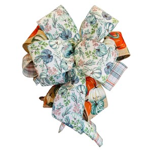 May include: A decorative bow featuring a variety of autumn-themed patterns. The bow incorporates fabrics with pumpkin and floral designs in shades of orange, teal, and cream. Plaid and burlap textures add to the fall aesthetic.