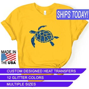May include: A yellow t-shirt with a blue glitter sea turtle design. The shirt has the text "SHIPS TODAY!" in a blue box at the top right corner. The text "MADE IN THE USA" is in a red, white, and blue box at the bottom left corner. The text "CUSTOM DESIGNED HEAT TRANSFERS" is in a purple box at the bottom center. The text "12 GLITTER COLORS" is in a purple box below the previous text. The text "MULTIPLE SIZES" is in a purple box below the previous text.