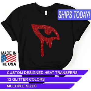May include: Black t-shirt with a red glitter eye dripping with glitter. The text "SHIPS TODAY!" is in a blue box at the top of the image. The text "MADE IN THE USA" is in a red, white, and blue box at the bottom left of the image. The text "CUSTOM DESIGNED HEAT TRANSFERS" is in a white box at the bottom of the image. The text "12 GLITTER COLORS" is in a white box below the previous text. The text "MULTIPLE SIZES" is in a white box below the previous text.