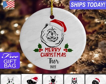 May include: White ceramic Christmas ornament with a black and white illustration of a Chow Chow dog wearing a red Santa hat. The ornament has the text "Merry Christmas Thor 2022" printed on it.