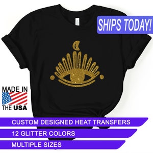 May include: Black t-shirt with a gold glitter eye design and the text "SHIPS TODAY!" in a blue box. The design features a crescent moon above the eye and a sunburst around the eye. The text "MADE IN THE USA" is in a red, white, and blue box. The text "CUSTOM DESIGNED HEAT TRANSFERS", "12 GLITTER COLORS", and "MULTIPLE SIZES" are in blue boxes.