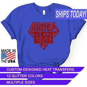 May include: A royal blue t-shirt with a red glitter design that says "Super Dad" in a diamond shape. The shirt is made in the USA and is available in multiple sizes and 12 glitter colors.