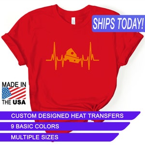 May include: Red t-shirt with a yellow heart beat graphic featuring a slice of cheese. The text "SHIPS TODAY!" is in a blue rectangle at the top of the image. The text "MADE IN THE USA" is in a blue rectangle at the bottom left of the image. The text "CUSTOM DESIGNED HEAT TRANSFERS" is in a blue rectangle at the bottom center of the image. The text "9 BASIC COLORS" is in a blue rectangle below the previous text. The text "MULTIPLE SIZES" is in a blue rectangle below the previous text.