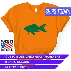 May include: Orange t-shirt with a green fish silhouette design. The shirt has the text "SHIPS TODAY!" in a blue box at the top right corner. The text "MADE IN THE USA" is in a red, white, and blue box at the bottom left corner. The text "CUSTOM DESIGNED HEAT TRANSFERS" is in a purple box at the bottom center. The text "9 BASIC COLORS" is in a purple box below the previous text. The text "MULTIPLE SIZES" is in a purple box below the previous text.
