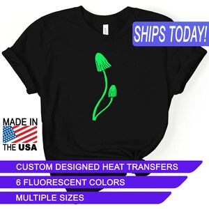 May include: Black t-shirt with a green mushroom graphic. The text "SHIPS TODAY!" is in a blue box at the top of the image. The text "MADE IN THE USA" is in a red, white, and blue box at the bottom left of the image. The text "CUSTOM DESIGNED HEAT TRANSFERS" is in a purple box at the bottom of the image. The text "6 FLUORESCENT COLORS" is in a purple box below the previous text. The text "MULTIPLE SIZES" is in a purple box below the previous text.