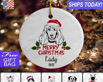 May include: White ceramic Christmas ornament with a black and white illustration of a dog wearing a red Santa hat. The ornament says "Merry Christmas Lady 2022".