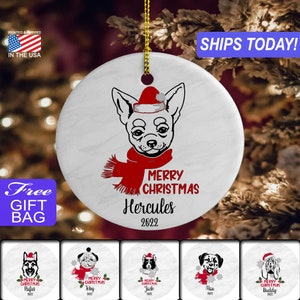 May include: White ceramic Christmas ornament with a black and white illustration of a chihuahua wearing a red Santa hat and scarf. The ornament says "Merry Christmas Hercules 2022".