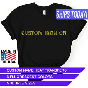 May include: Black t-shirt with the text "CUSTOM IRON ON" in yellow. The shirt is made in the USA and features custom name heat transfers in 6 fluorescent colors and multiple sizes.