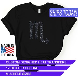 May include: Black t-shirt with a glitter Scorpio zodiac sign. The shirt says "SHIPS TODAY!" and "CUSTOM DESIGNED HEAT TRANSFERS", "12 GLITTER COLORS", and "MULTIPLE SIZES".
