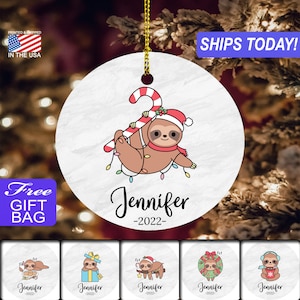 May include: A white ceramic Christmas ornament featuring a cartoon sloth holding a candy cane and hanging from Christmas lights. The ornament is personalized with the name "Jennifer" and the year "2022".