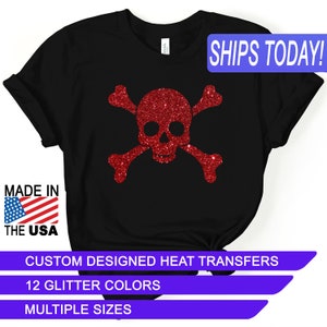 May include: Black t-shirt with a red glitter skull and crossbones design. The text "SHIPS TODAY!" is in a blue box at the top of the image. The text "MADE IN THE USA" is in a red, white, and blue box at the bottom left of the image. The text "CUSTOM DESIGNED HEAT TRANSFERS" is in a white box at the bottom of the image. The text "12 GLITTER COLORS" is in a white box below the previous text. The text "MULTIPLE SIZES" is in a white box below the previous text.