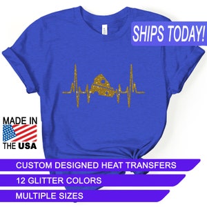 May include: A royal blue t-shirt with a gold glitter design of a heart beat with a wedge of cheese in the middle. The text "SHIPS TODAY!" is in a white rectangle with a blue border. The text "MADE IN THE USA" is in a red, white, and blue rectangle. The text "CUSTOM DESIGNED HEAT TRANSFERS" is in a white rectangle with a purple border. The text "12 GLITTER COLORS" is in a white rectangle with a purple border. The text "MULTIPLE SIZES" is in a white rectangle with a purple border.