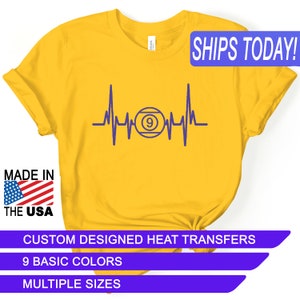 May include: Yellow t-shirt with a purple heartbeat design featuring a pool ball with the number 9. The text "SHIPS TODAY!" is in a blue box at the top of the image. The text "MADE IN THE USA" is in a red, white, and blue box at the bottom left of the image. The text "CUSTOM DESIGNED HEAT TRANSFERS" is in a purple box at the bottom of the image. The text "9 BASIC COLORS" is in a purple box below the previous text. The text "MULTIPLE SIZES" is in a purple box below the previous text.