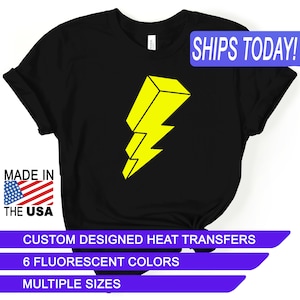 May include: Black t-shirt with a yellow lightning bolt graphic. The text "SHIPS TODAY!" is in a blue box at the top of the image. The text "MADE IN THE USA" is in a red, white, and blue box at the bottom left of the image. The text "CUSTOM DESIGNED HEAT TRANSFERS" is in a purple box at the bottom of the image. The text "6 FLUORESCENT COLORS" is in a purple box below the previous text. The text "MULTIPLE SIZES" is in a purple box below the previous text.