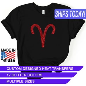 May include: Black t-shirt with a red glitter Aries zodiac sign. The text "SHIPS TODAY!" is in a blue box at the top of the image. The text "MADE IN THE USA" is in a red, white, and blue box at the bottom left of the image. The text "CUSTOM DESIGNED HEAT TRANSFERS" is in a purple box at the bottom of the image. The text "12 GLITTER COLORS" is in a purple box below the previous text. The text "MULTIPLE SIZES" is in a purple box below the previous text.