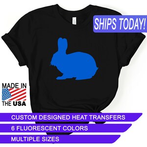 May include: Black t-shirt featuring a blue rabbit silhouette. The shirt includes the text "SHIPS TODAY!" and "MADE IN THE USA". Additional text reads "CUSTOM DESIGNED HEAT TRANSFERS", "6 FLUORESCENT COLORS", and "MULTIPLE SIZES".