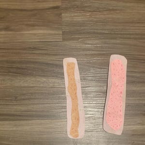 May include: Two decorative paper cutouts. One is light brown with gold glitter accents and the other is pink with red glitter accents. Both are on a light pink background.
