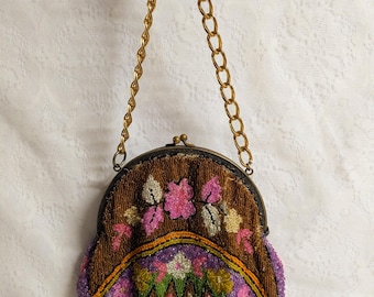 May include: A small, rounded coin purse featuring intricate beadwork in shades of brown, purple, pink, green, and white. The purse has a metal frame with a clasp closure and a gold-toned chain handle. The surface displays floral and geometric patterns.