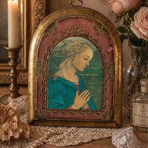 Pode incluir: Uma obra de arte emoldurada em arco com um retrato em estilo renascentista de uma mulher em um vestido azul, com as mãos juntas em oração. A moldura é dourada com uma borda rosa e verde. Uma vela acesa e rosas ao fundo.