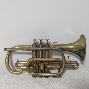 May include: A vintage brass cornet with four valves and a bell. The cornet has a worn, aged finish and is in good condition.