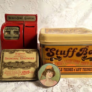 May include: A selection of antique items: a red toy cash register, a yellow "Stuff Box" tin, a small round tin with a woman's portrait, and a tin of "Regesan Bronchial Lozenges" from Nottingham.