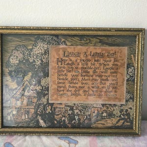 Könnte beinhalten: Gerahmtes Vintage-Kunstwerk mit einem goldfarbenen, verzierten Rahmen. Das Kunstwerk zeigt eine detaillierte Schwarz-Weiß-Illustration einer Dorfszene und einen gedruckten Text mit der Aufschrift "Laugh a Little Bit!"
