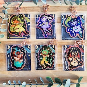 May include: Six colorful keychains with different characters and designs. Each keychain features a character with a unique style and personality. The keychains are made of clear acrylic and have a shiny, holographic finish. The keychains are perfect for adding a touch of personality to your keys, bags, or backpacks.