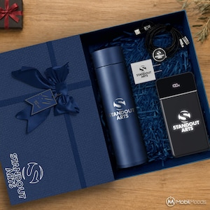 Peut inclure: Un coffret cadeau bleu marine contenant une bouteille isotherme bleu marine assortie, une batterie externe noire avec affichage numérique 100 %, un chargeur mural blanc et un câble de charge noir. Tous portent le logo Standout Arts en blanc.