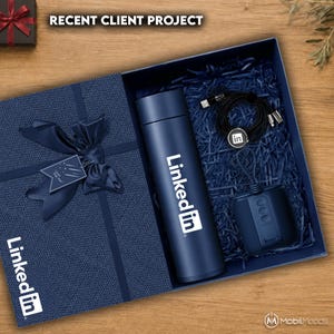 May include: A navy blue gift box containing a matching navy blue vacuum insulated bottle with the LinkedIn logo, a black circular charging cable with a LinkedIn logo tag, and a navy blue square speaker, all nestled in dark blue paper shred.