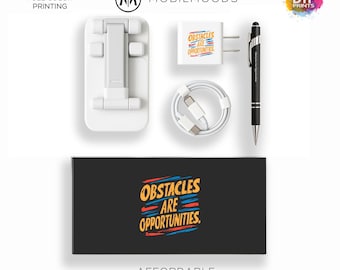 Pode incluir: Um conjunto de presentes acessível com um suporte de telefone branco, carregador, cabo, caneta e uma caixa com o texto "OBSTACLES ARE OPPORTUNITIES". Impressão a cores.