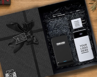 Könnte beinhalten: Eine schwarze Geschenkbox mit strukturiertem Deckel, schwarzer Schleife und einem Anhänger mit der Aufschrift "Just For You". Darin befinden sich ein schwarzer Stift, ein weißes Ladegerät, eine schwarze kabellose Ladestation und eine weiße Powerbank.