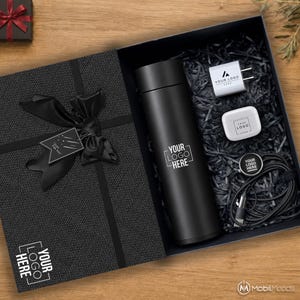 Peut inclure: Un coffret cadeau noir contenant un gobelet isotherme noir mat, un adaptateur secteur blanc, des écouteurs sans fil blancs et un câble de charge noir, tous portant le texte YOUR LOGO HERE. Le couvercle a un ruban noir et une étiquette Just For You.