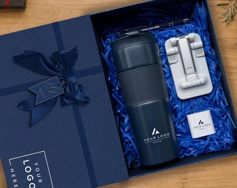 Könnte beinhalten: Eine marineblaue Geschenkbox mit einem passenden marineblauen Isolierbecher mit strukturiertem Griff, einem silbernen faltbaren Handyhalter, einem weißen Wandladegerät und einem schwarzen Stift. Der Deckel hat eine marineblaue Schleife.