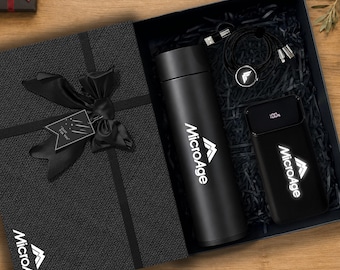 May include: A black gift box containing a black vacuum insulated bottle, a black power bank with a digital display showing 100%, and a black charging cable. The box features a black ribbon, a tag reading Just For You, and the MicroAge logo.
