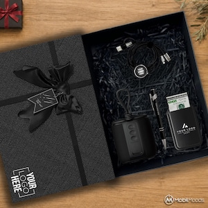 Peut inclure: Un coffret cadeau noir à couvercle texturé, orné d'un nœud en ruban noir et d'une étiquette Just For You. À l'intérieur, du papier noir entoure un câble de charge, une enceinte, un stylo et un porte-cartes noir contenant un billet de 100 dollars.