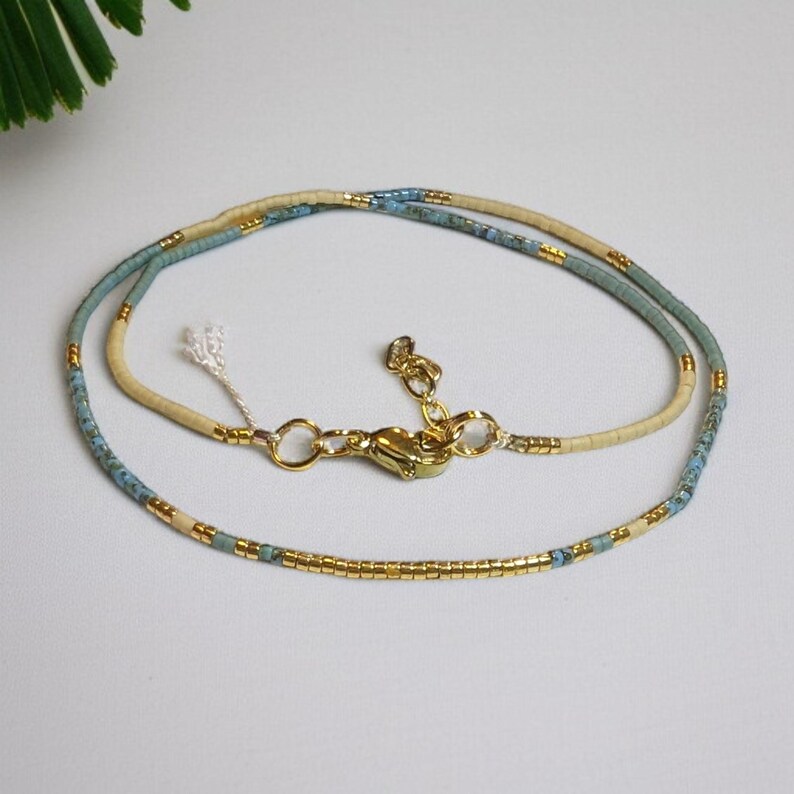 May include: A delicate double-strand necklace with gold and blue beads. The necklace has a gold clasp and a small white tassel.