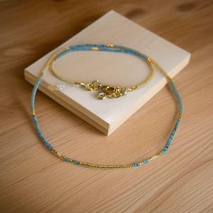 May include: A delicate necklace made with tiny blue and gold beads. The necklace is layered with two strands of beads, creating a subtle ombre effect.