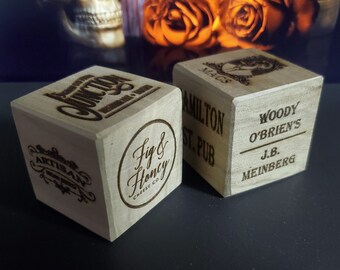May include: Two wooden blocks with engraved text. The first block has the text "Fig & Honey Cheese Co." and "Artisan" on it. The second block has the text "Hamilton St. Pub", "Woody O'Brien's", and "J.B. Meinberg" on it.