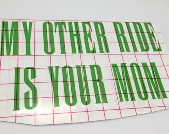 May include: Green vinyl lettering on a white background with a grid pattern. The lettering reads "My other ride is your mom."