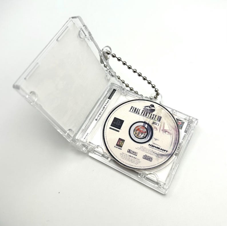 May include: A clear plastic keychain case with a silver chain. The case holds a silver PlayStation game disc with the text "FINAL FANTASY VII DISC 1" and the logo for SquareSoft.