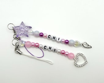 May include: Two beaded phone charms with the name "CHI" spelled out in white letters. One charm has a purple star and a silver wing charm. The other charm has a pink heart charm.