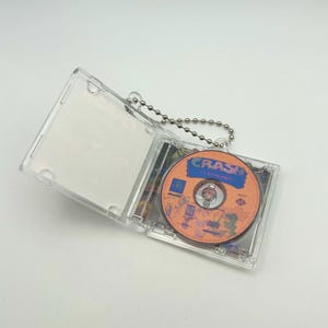 May include: A clear plastic keychain with a small CD inside. The CD is orange and has the words "Crash Bandicoot" printed on it.
