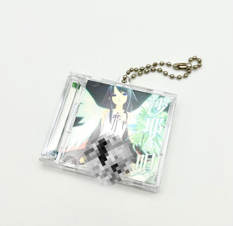 May include: A clear plastic CD case keychain featuring an anime-style illustration of a woman with long dark hair and blue eyes. The artwork has a fantasy theme with green and white accents. A silver ball chain is attached for hanging.